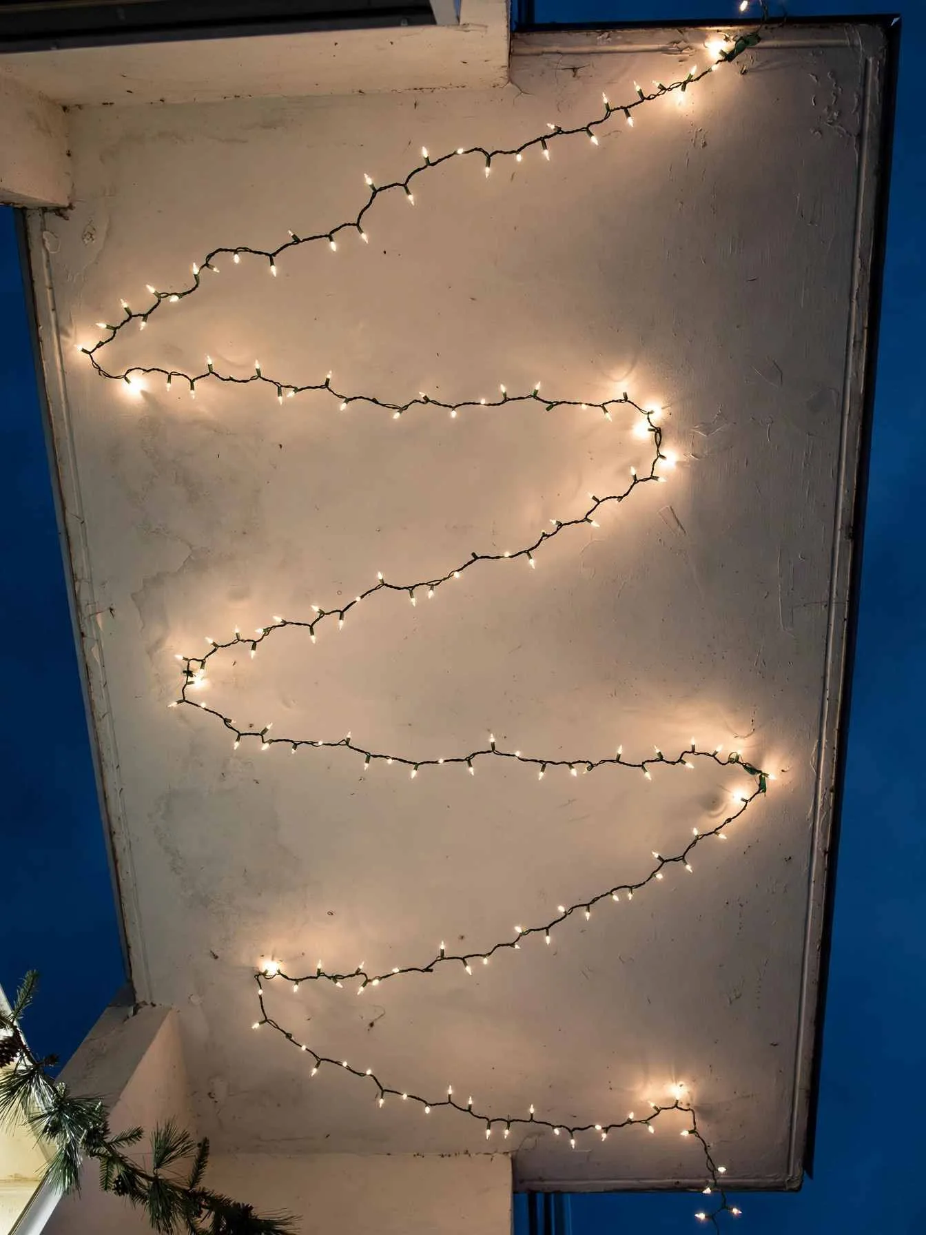 Warm-white LED string lights zigzagging overhead in loose S-curves against a dark blue evening sky above a small balcony