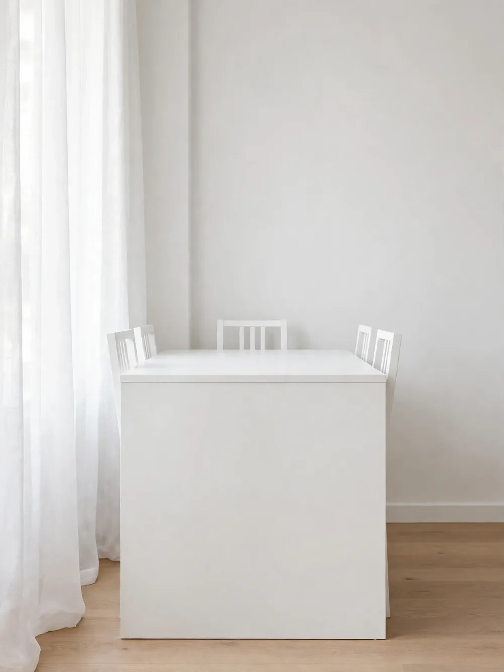 Compact white dining table with four chairs pushed completely underneath, reading as one cube